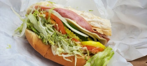 A sub sandwich filled with layers of lettuce, tomato, green pepper, ham, and cheese, served in a soft hoagie roll.