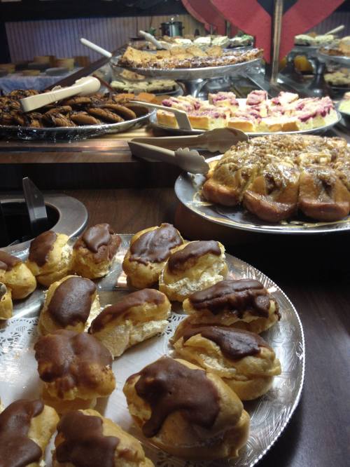 A variety of desserts displayed on trays, including chocolate-covered pastries and assorted baked goods in the background.