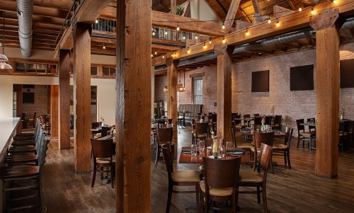 A spacious restaurant interior with wooden beams, tables set for dining, and warm lighting.