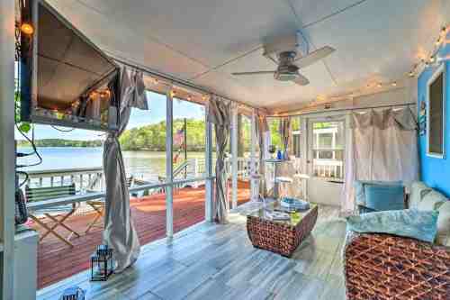 Cozy sunroom with a view of the water, featuring a wicker coffee table, curtains, and string lights.