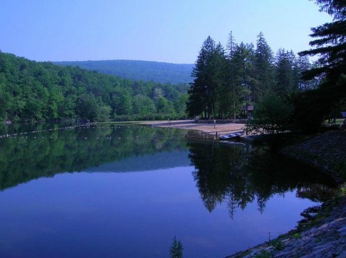 A serene lake surrounded by lush green trees and mountains, reflecting the landscape in calm waters.