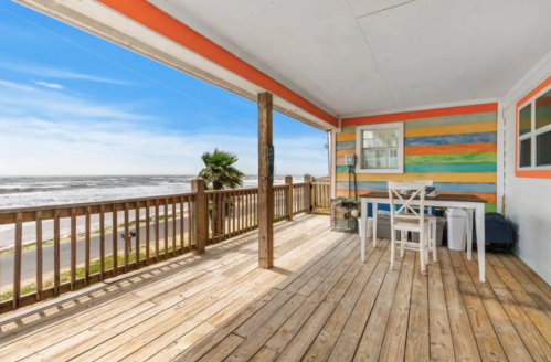 A bright, colorful deck overlooking the ocean, featuring a table and chairs with a clear blue sky in the background.