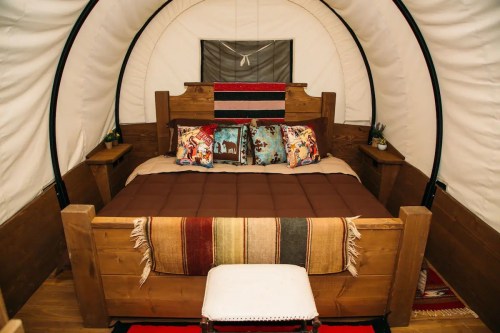 Cozy interior of a glamping tent featuring a wooden bed with decorative pillows and a colorful blanket.