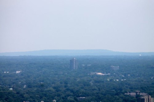 A hazy view of a city skyline with green trees and distant hills in the background.