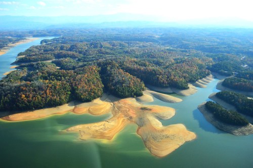 Aerial view of a serene lake surrounded by colorful autumn foliage and sandy shores.