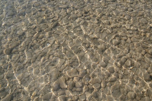 Clear water over smooth, rounded pebbles, creating a shimmering effect on the surface.