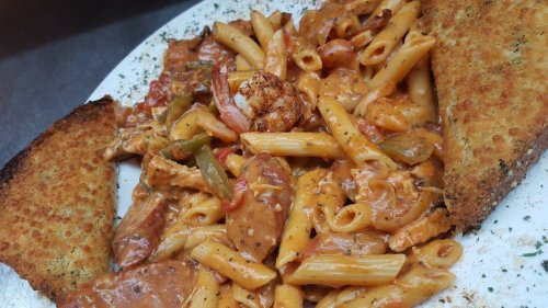 A plate of creamy pasta with shrimp, chicken, and bell peppers, served with two slices of toasted garlic bread.