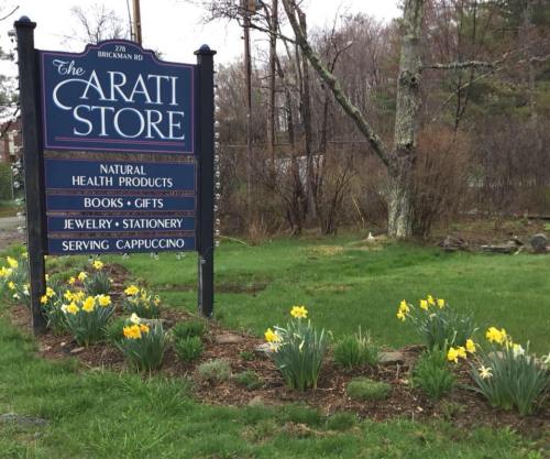 Sign for "The Carati Store" featuring natural health products, books, gifts, and yellow daffodils in the foreground.
