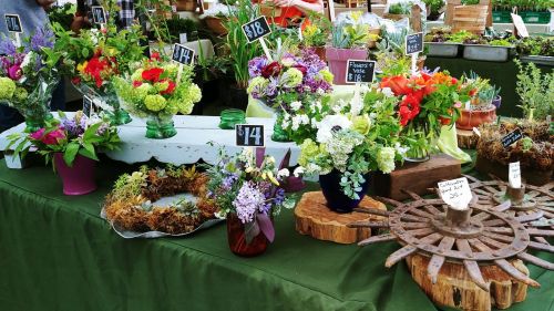 A vibrant flower market display with various bouquets, potted plants, and decorative items on a green tablecloth.