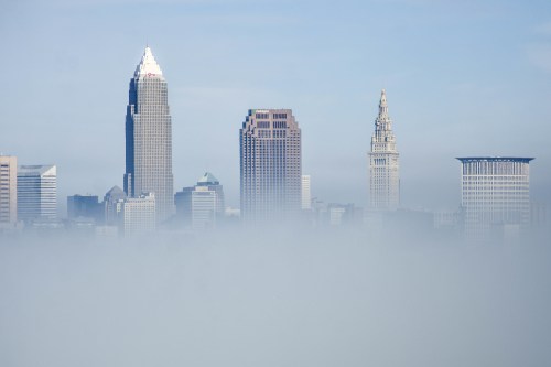Cleveland skyline partially obscured by fog, featuring tall buildings and a clear blue sky above.