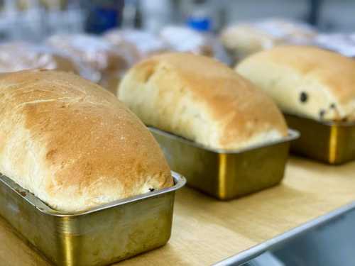 Three freshly baked loaves of bread in golden metal pans on a wooden surface.