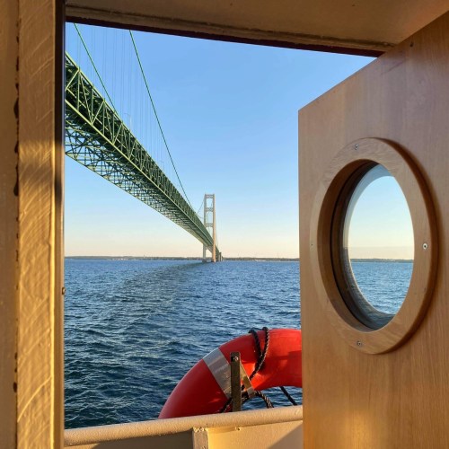 View from a boat showing a bridge in the distance, framed by a door and a life ring on the side.