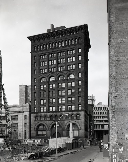 Historic black-and-white photo of a tall brick building with arched windows, surrounded by construction sites.
