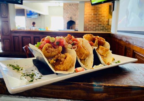 Three crispy tacos filled with fried chicken, topped with salsa and green onions, served on a white plate.
