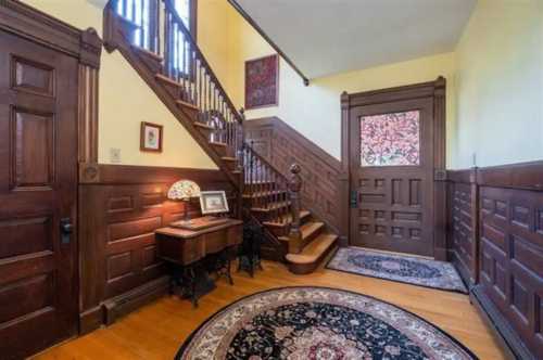 A vintage entryway featuring a wooden staircase, decorative rugs, and warm yellow walls.