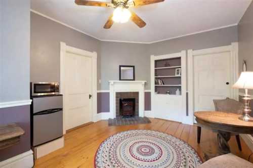 Cozy room with a ceiling fan, a small fridge, a fireplace, bookshelves, and a round rug on wooden floors.