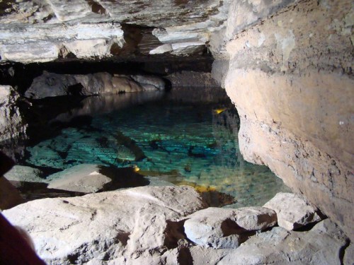 A serene underground cave with clear blue water reflecting the rocky walls.