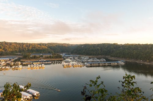 A serene view of a marina at sunrise, surrounded by lush green hills and calm waters.