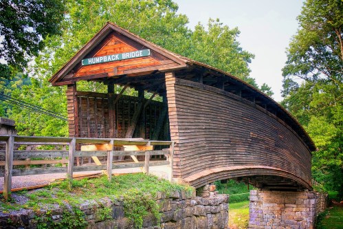 A wooden covered bridge with a curved roof, surrounded by trees, labeled "Humpback Bridge."