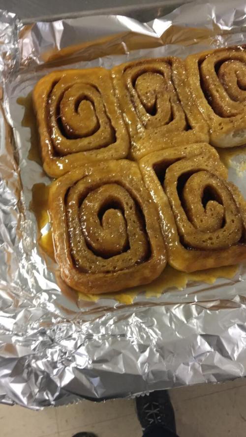 Freshly baked cinnamon rolls drizzled with caramel, arranged in a foil-lined tray.