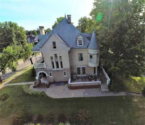 Aerial view of a large, historic house with a turret, surrounded by greenery and a paved patio.