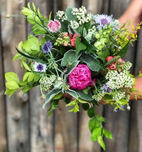 A vibrant bouquet of mixed flowers and greenery held against a rustic wooden background.