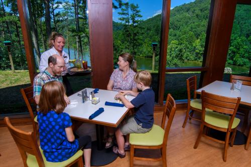 A family enjoys a meal at a restaurant with large windows overlooking a scenic view of trees and mountains.