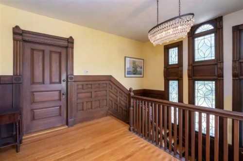 A well-lit staircase with wooden paneling, a chandelier, and a door leading to another room.