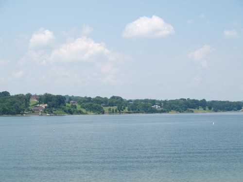 A serene lake view with lush green hills and a clear blue sky dotted with fluffy white clouds.