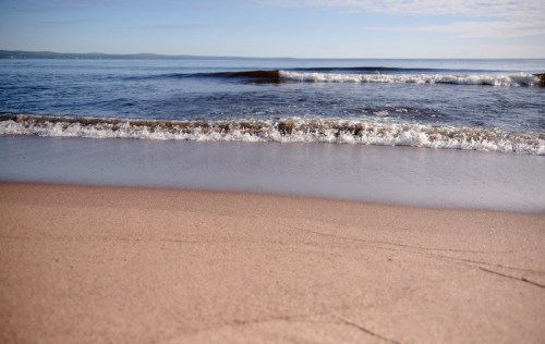 Gentle waves lapping at a sandy beach under a clear blue sky.