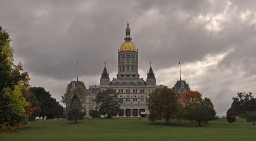 Connecticut State Capitol building with a golden dome, surrounded by trees and a cloudy sky.