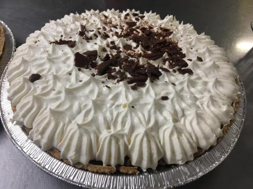 A creamy pie topped with whipped cream and chocolate shavings in a silver pie tin.