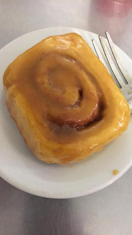 A glazed cinnamon roll on a white plate with a fork beside it.
