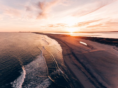 Aerial view of a serene beach at sunset, with gentle waves and a colorful sky reflecting on the water.