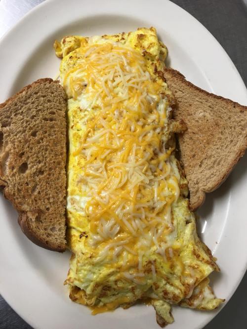 A large cheese omelette topped with shredded cheese, served with two slices of toasted bread on a white plate.