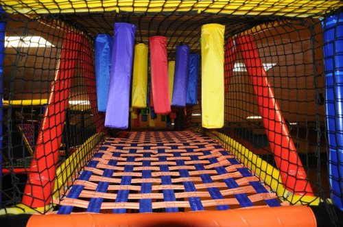 Colorful indoor play structure with soft, padded obstacles and a netted enclosure.