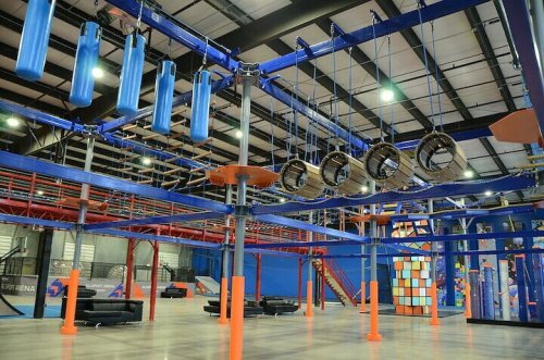 Indoor adventure park featuring obstacle courses, hanging tires, and colorful climbing structures.