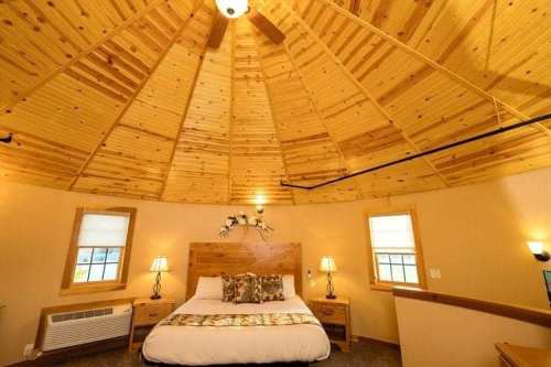Cozy circular bedroom with wooden ceiling, a large bed, bedside tables, and warm lighting.