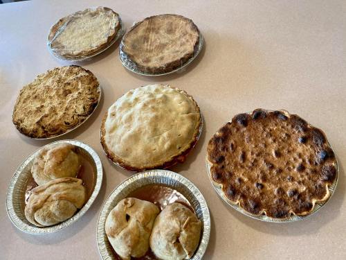 A variety of baked pies on a countertop, including fruit and savory options, some with golden crusts and others slightly burnt.
