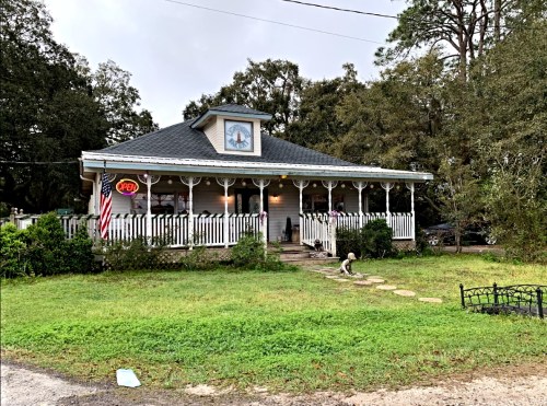 A charming house with a porch, "OPEN" sign, and a small garden, surrounded by trees.