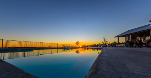 Sunset over a tranquil pool, with lounge chairs and a rustic building in the background, creating a serene atmosphere.
