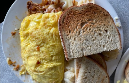 A plate with a fluffy omelet, two slices of toasted bread, and a side of potatoes.