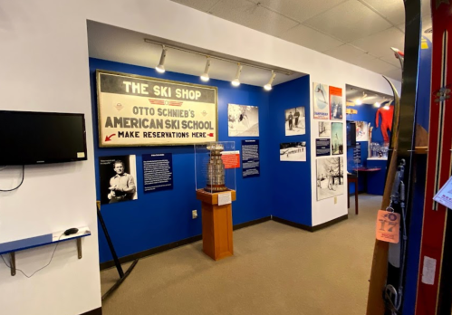 Interior of a ski shop exhibit featuring historical photos and a sign for Otto Schneid's American Ski School.