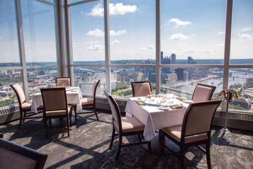 Elegant restaurant interior with tables set for dining, featuring large windows showcasing a panoramic city view.