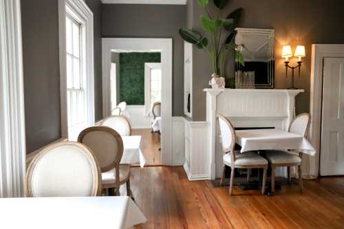 A cozy restaurant interior featuring elegant chairs, white tables, and green accents on the walls.