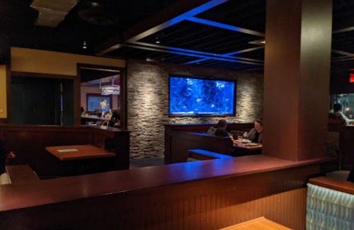 A dimly lit restaurant interior featuring a large aquarium and wooden seating areas.