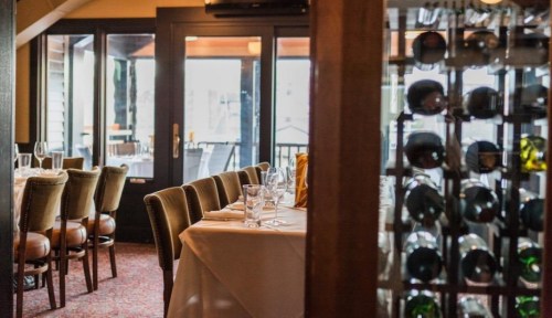 A cozy restaurant interior with a table set for dining and a wine rack in the foreground.