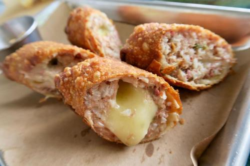 Crispy fried rolls filled with melted cheese and savory meat, served on a tray with a dipping sauce.