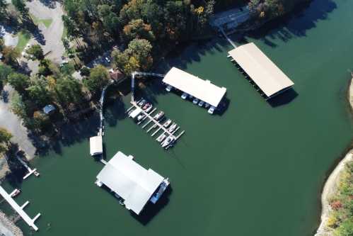 Aerial view of a marina with several boat docks and covered slips surrounded by trees and calm water.