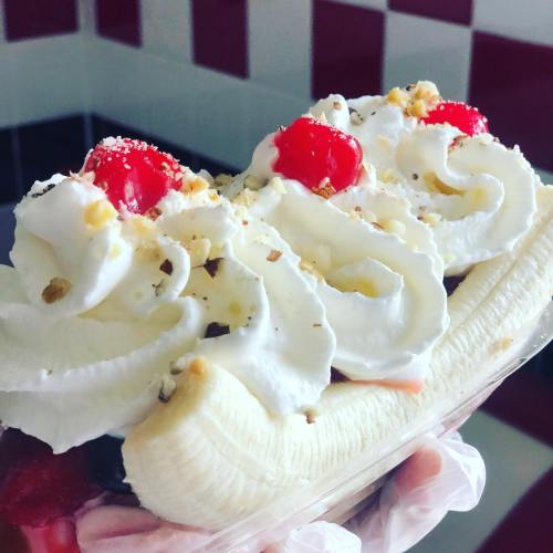 A close-up of a banana split topped with whipped cream, cherries, and nuts in a clear container.